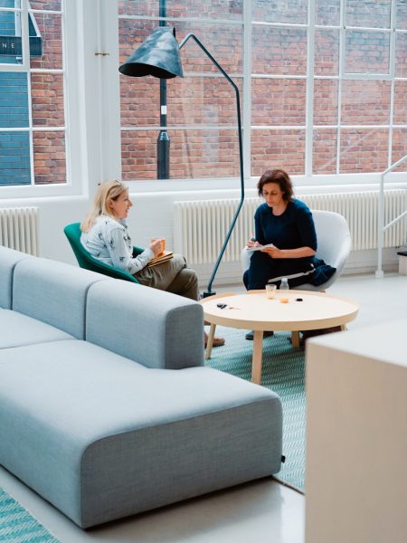 two woman sits on sofa chairs inside house