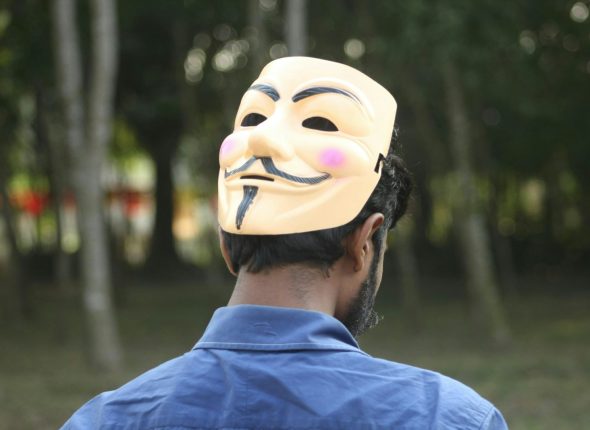 Man wearing an anonymous mask looking away.