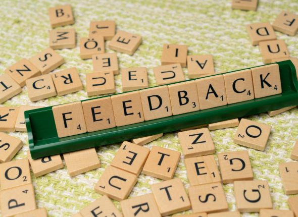 Wooden letter tiles spelling 'feedback' on a green rack, representing communication and evaluation.