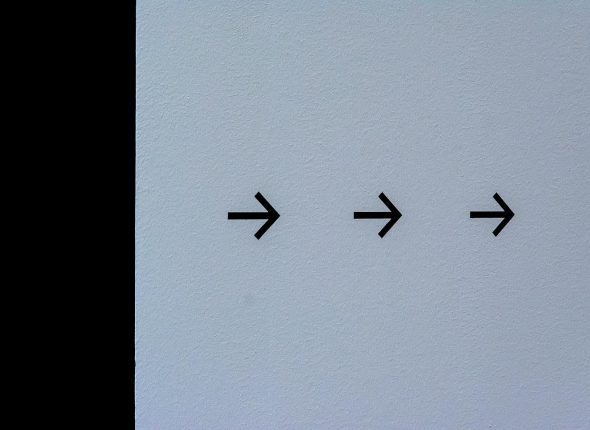 Simple white wall featuring three black arrows pointing right, conveying direction.