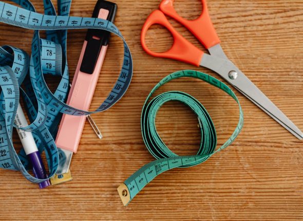 Top view of sewing tools including scissors, tape measures, and a stapler on a wooden surface.
