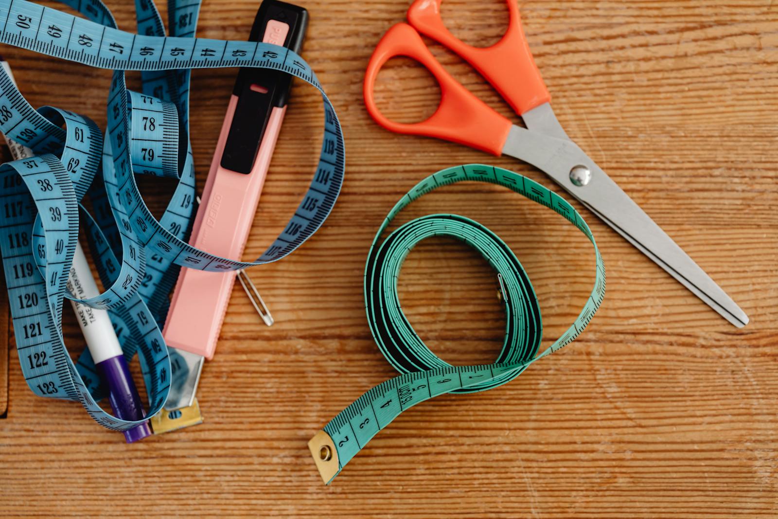 Top view of sewing tools including scissors, tape measures, and a stapler on a wooden surface.