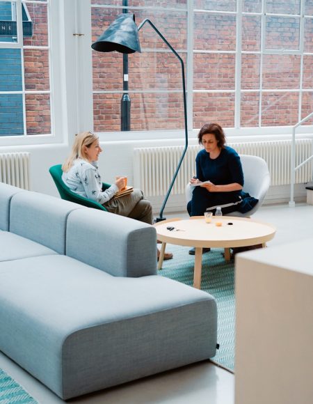 two woman sits on sofa chairs inside house